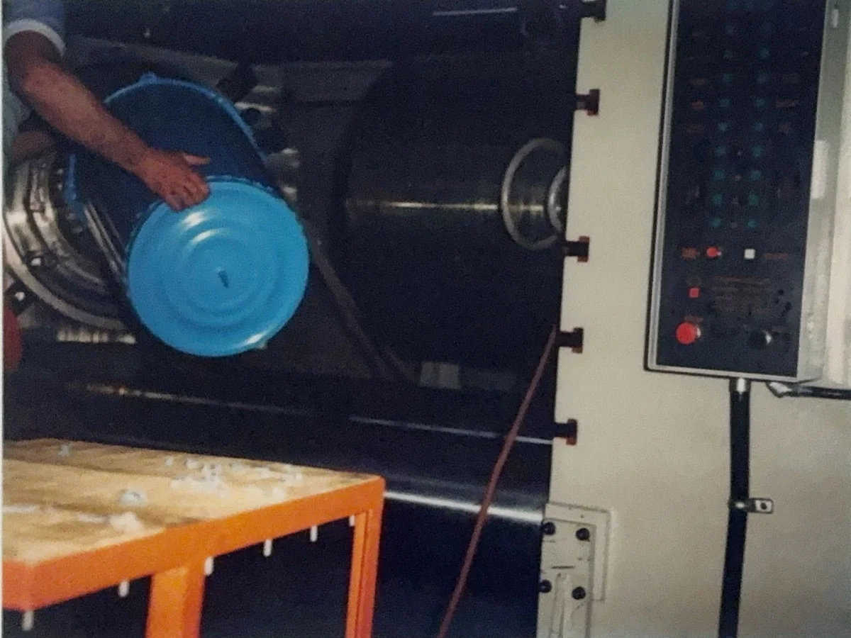 Operario sacando de la máquina una tina de plástico azul recién inyectada, en los primeros años de la planta
