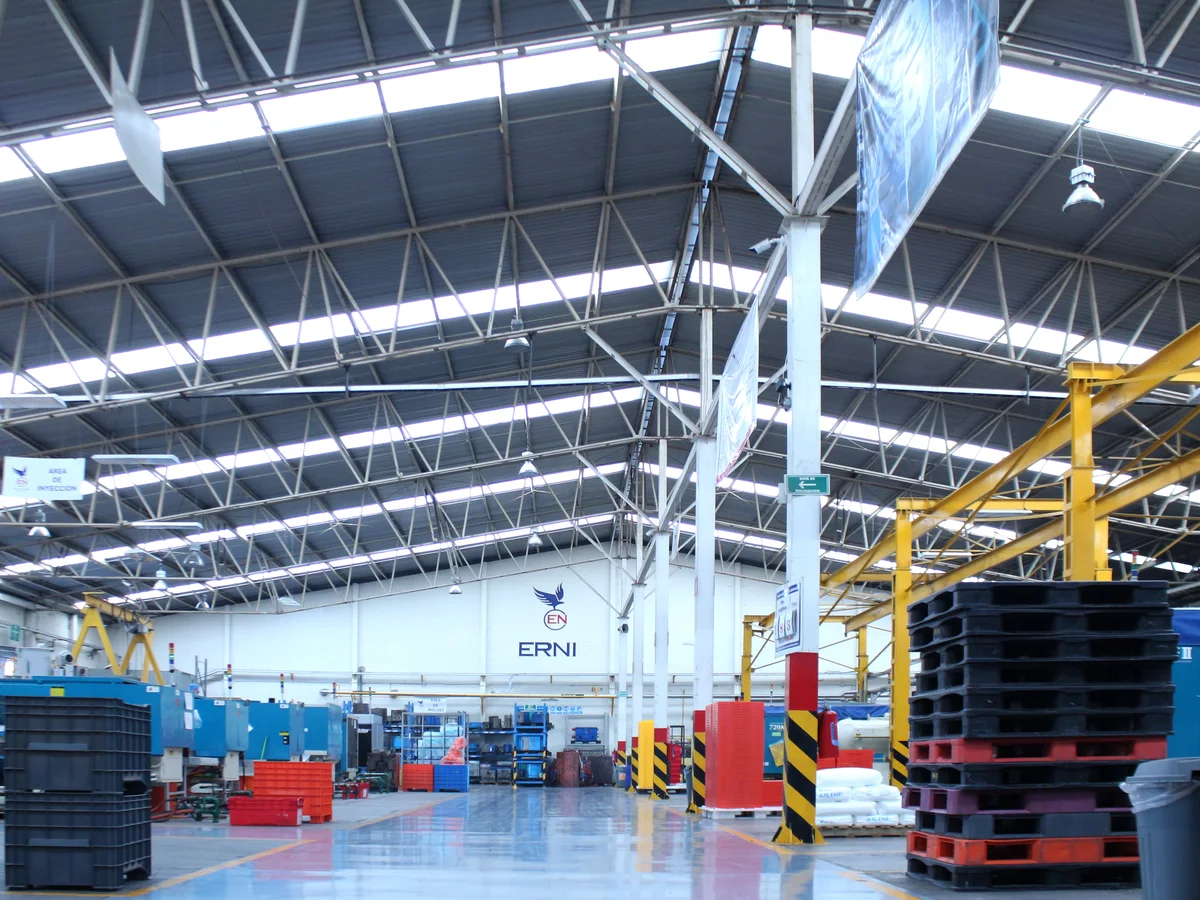 Interior de la planta ERNI, con las máquinas de inyección y estibas de tarimas bajo el logotipo ERNI
